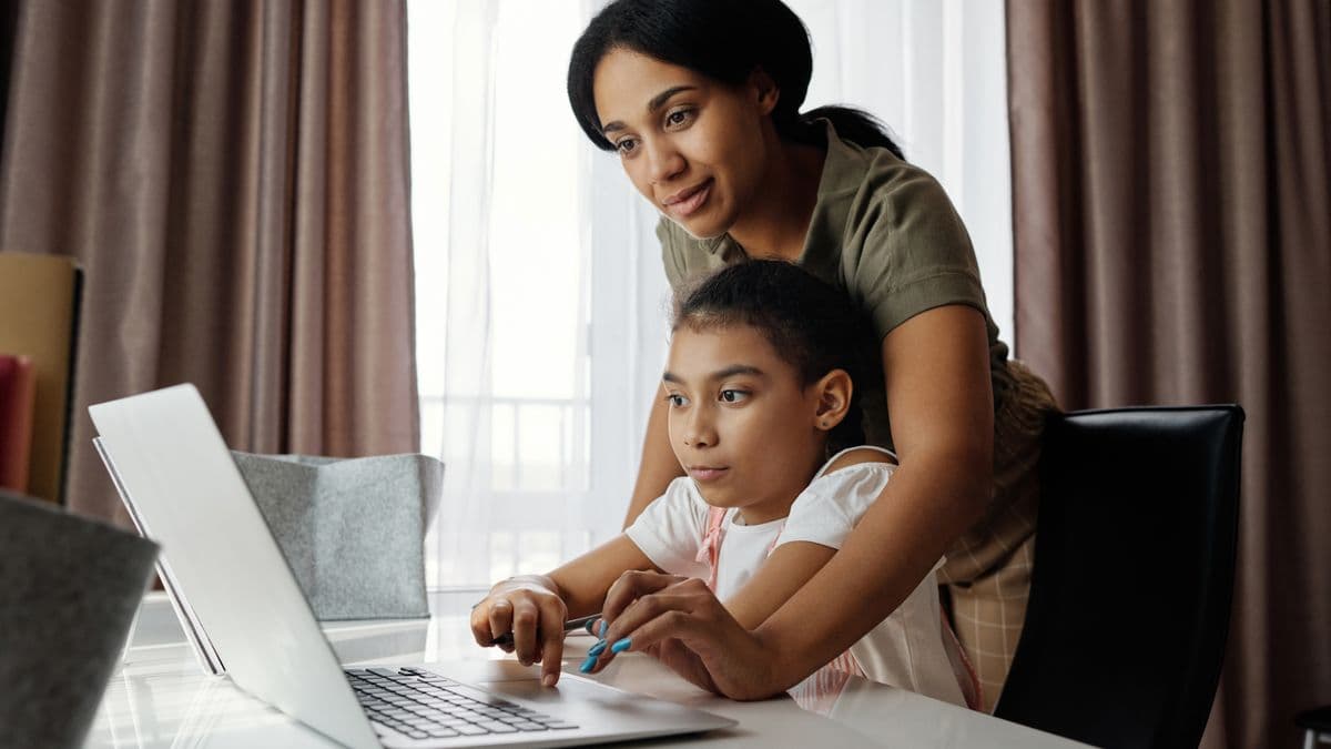 Parent guiding a child through communication and learning activities using a laptop at home